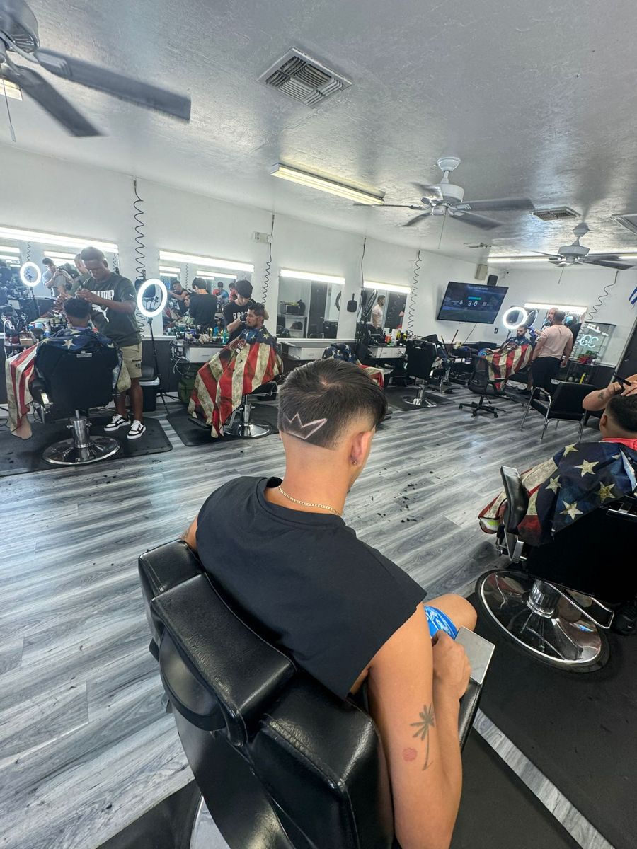 Interior de la barbería con sillas de barbero, espejos y aros de luz; un cliente sentado de espaldas